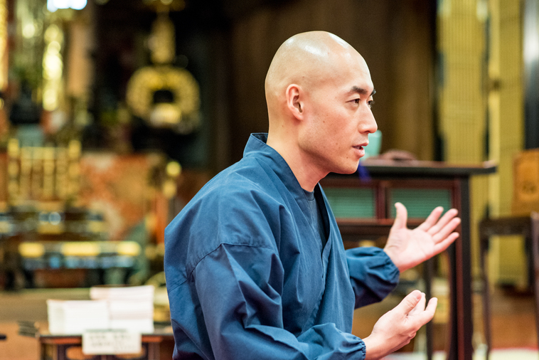 【写真】光明寺の本堂で真剣な表情でインタビューに答えるまつもとしょうけいさん