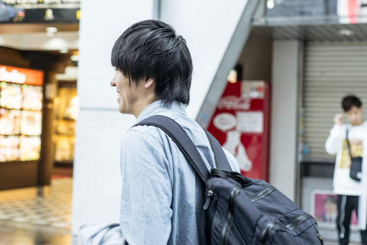 【写真】屋外を歩くいまいさんの横顔。笑みを浮かべている。