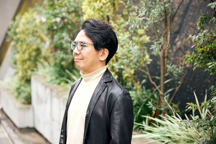 【写真】屋外で左の方向を見つめるまつむらさん