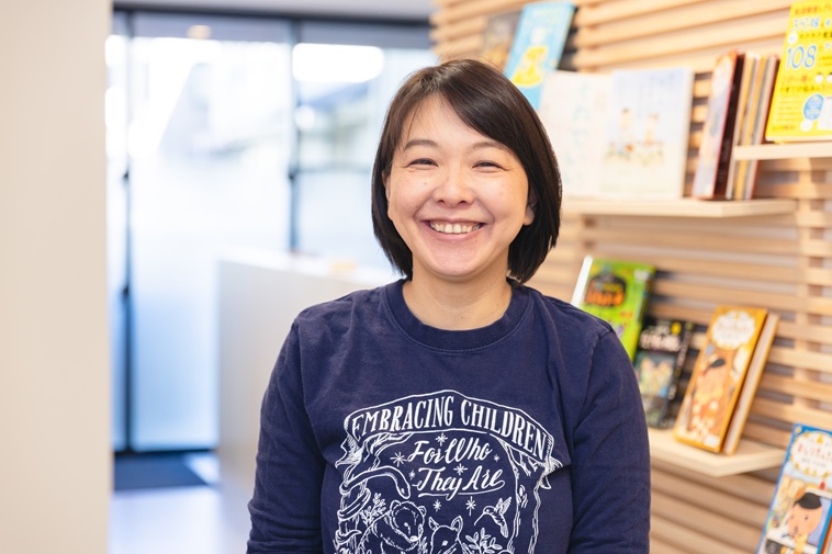 【写真】スタッフTシャツを着てカメラを見つめて微笑むたなかせんせい