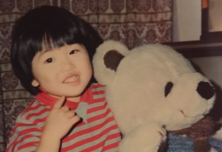 【写真】幼少期のふじきさん。大きな熊のぬいぐるみと一緒に笑顔でうつっている